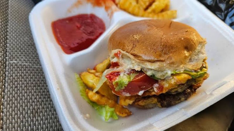 A burger with tomato and lettuce next to crinkle fries and ketchup in a foam tray