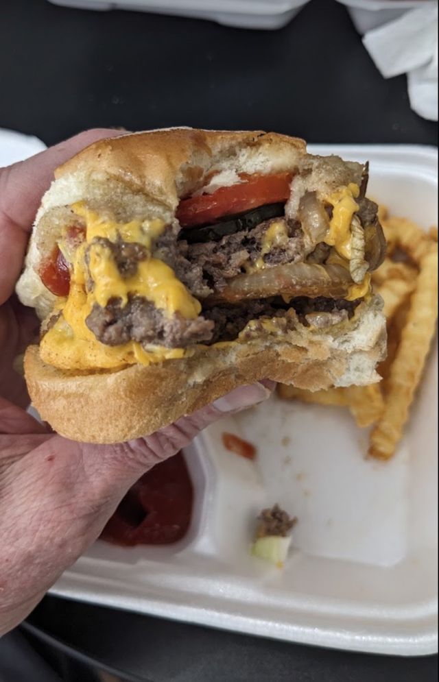 A bitten burger showing stacked patties, melted cheese, grilled onion, tomato and pickle