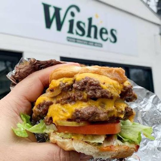 A triple burger with melted cheese held up in front of the Wishes sign