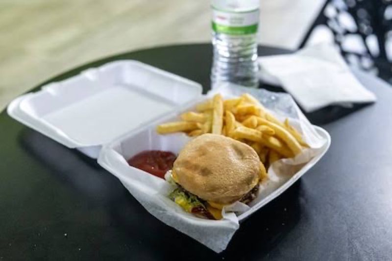 A burger, fries and ketchup in an open foam clamshell on a dark table