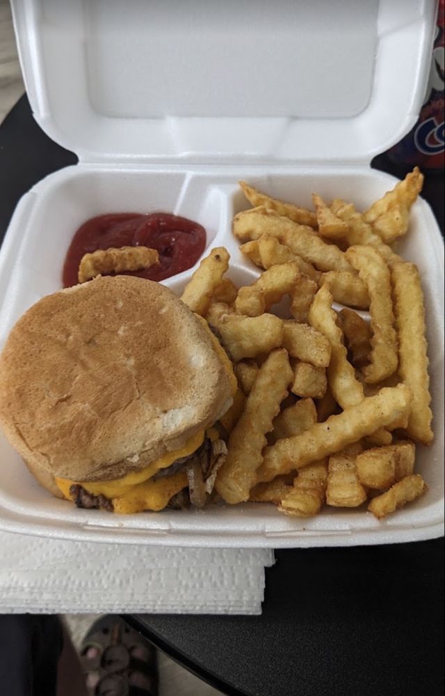 A burger with melted cheese and a pile of crinkle-cut fries in a foam clamshell with ketchup